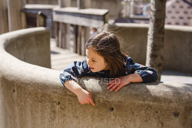 Ein kleines Mädchen lehnt sich an einem windigen, sonnigen Tag über eine geschwungene Steinmauer — Stockfoto