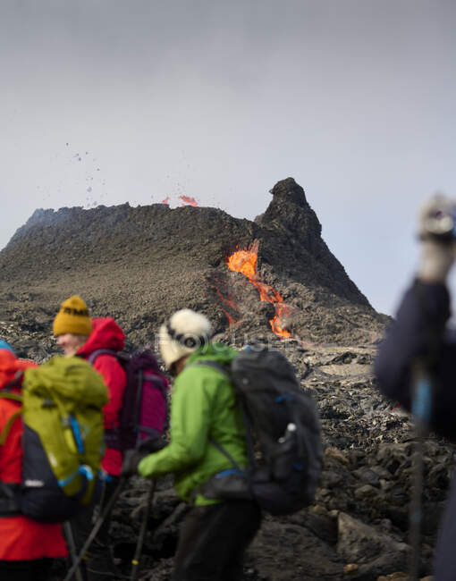 Unrecognizable travelers hiking near active erupting volcano — Stock Photo