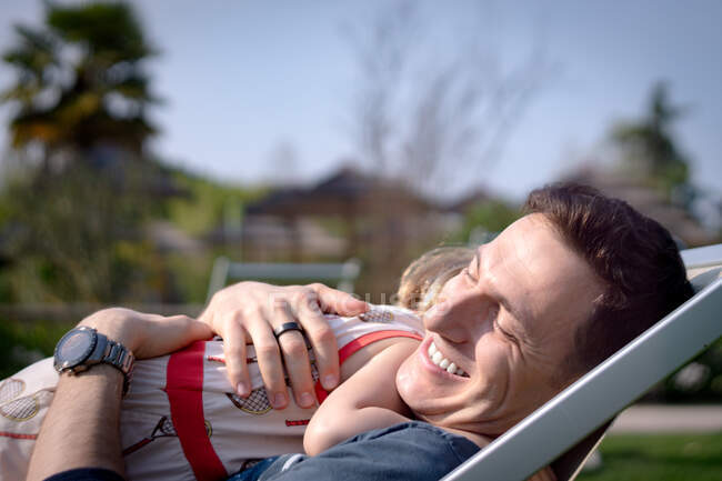 Jovem abraçando seu pai enquanto se senta na cadeira lounge no parque — Fotografia de Stock