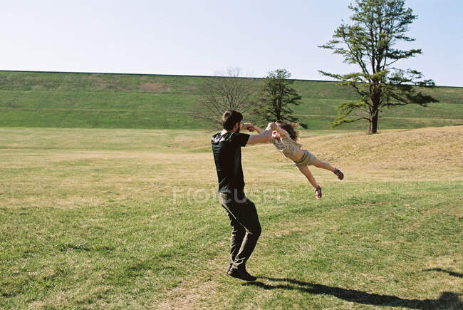 A little girl and her father playing in a grassy field by a dike — Stock Photo