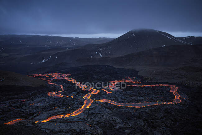 Vista severa della lava ignea che scorre sul pendio roccioso attivo del vulcano negli altopiani in serata — Foto stock