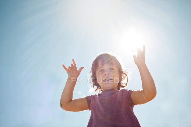 Menina segurando as mãos para o sol em um céu azul — Fotografia de Stock