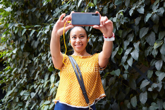 Joven mujer tomando una selfie con su teléfono inteligente en la calle - foto de stock