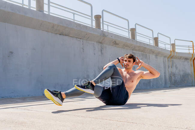 Junger Mann macht mittags Sit-ups ohne Hemd auf der Straße — Stockfoto