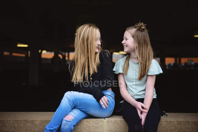 Dos muchachas felices del tween que se sientan en una pared de ladrillo juntas. - foto de stock