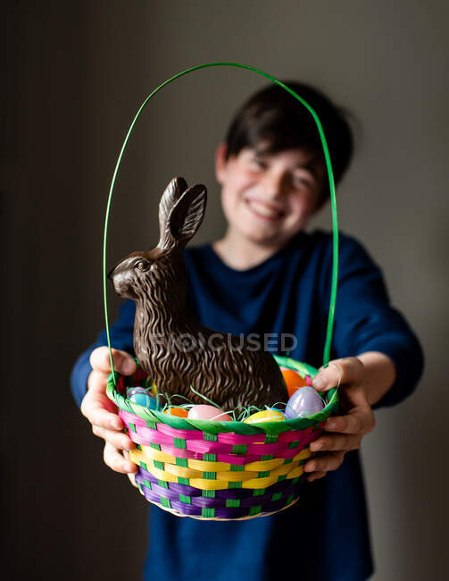 Jovem menino feliz segurando cesta de Páscoa cheia de ovos e coelho de chocolate — Fotografia de Stock