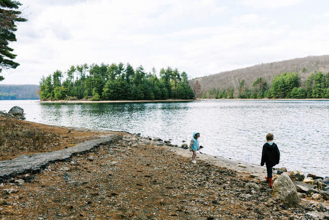 Due bambini che giocano sulla spiaggia rocciosa di un lago circondato dalla foresta — Foto stock