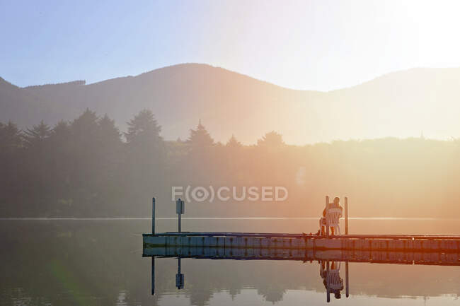 Uomo seduto su un molo vicino a un lago al tramonto. — Foto stock