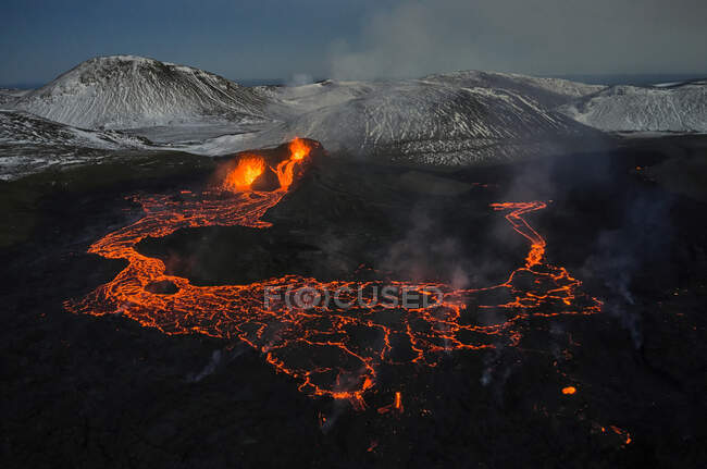 Atemberaubender Drohnenblick auf heiße, orangefarbene Lava, die während eines Vulkanausbruchs in bergigem Gelände fließt — Stockfoto