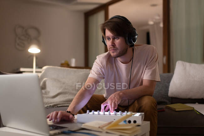 Homme dans les écouteurs en utilisant la table d'harmonie et ordinateur portable pour créer de la musique sur le canapé à la maison — Photo de stock