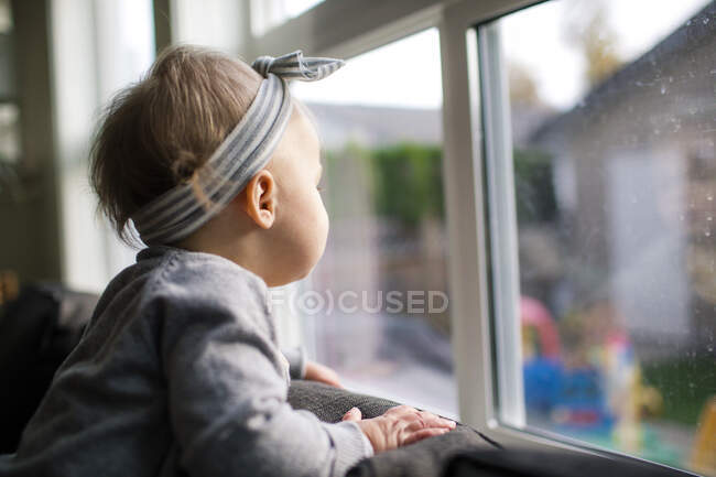 Side view of young girl looking out the window into her backyard. — Stock Photo