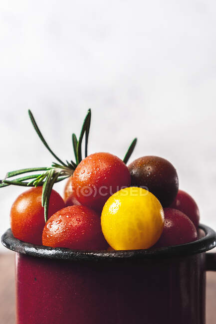 Uma caneca de metal cheia de diferentes tomates cereja coloridos com alecrim em uma mesa de madeira. Comida mediterrânea. Vegan e comida orgânica. Comida típica de verão — Fotografia de Stock