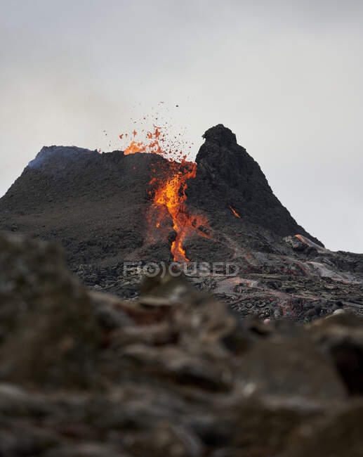 Vista severa del volcán en erupción con lava ardiente y vapor que fluye en la pendiente rocosa bajo el cielo nublado gris - foto de stock