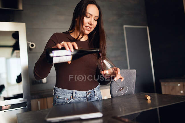 Belle femme brune se verse du vin rouge dans sa cuisine — Photo de stock