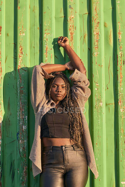 Schwarze Frau mit Zöpfen und urbaner Kleidung posiert und blickt in die Kamera — Stockfoto