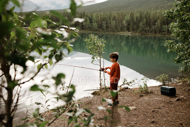Jeune garçon portant pêche rouge dans un lac vert le matin — Photo de stock