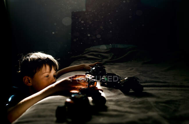 Мальчик в голубой рубашке играет с машинами на кровати в спальне — стоковое фото