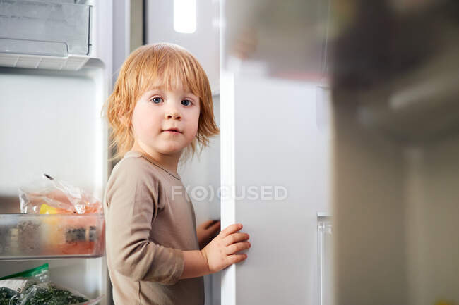 Red-haired child looks into the refrigerator. looking for food — Stock Photo