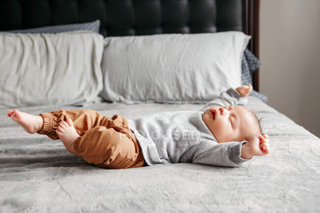 Cute funny newborn baby boy sleeping on bed at home and stretching. — Stock Photo