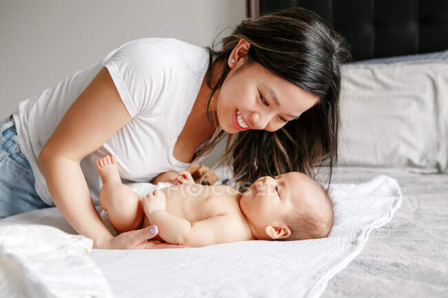 Chinese Asian busy mother changing diaper clothes for newborn infant baby son. Home lifestyle authentic natural family moment and morning routine. Ethnic diversity. Health and care for baby. — Stock Photo