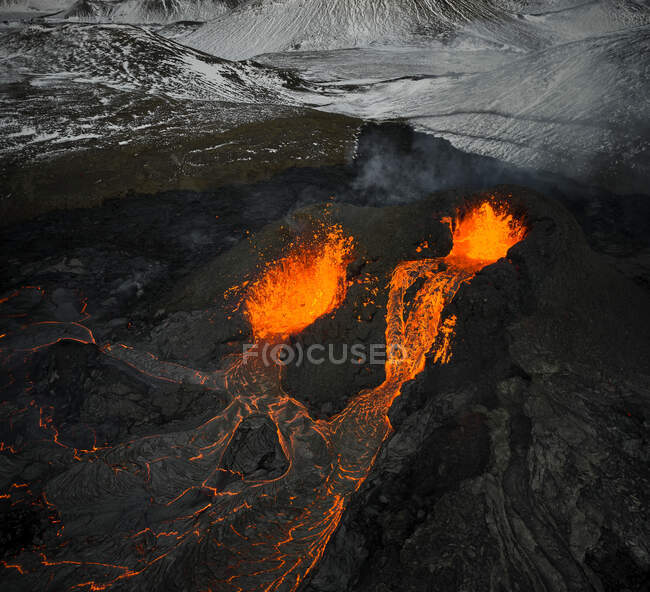 Vista aérea da montanha vulcânica rochosa que entra em erupção com magma laranja quente nas terras altas no inverno — Fotografia de Stock