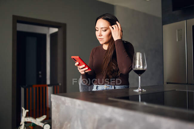 Brünette Frau trinkt Rotwein und hält ein Handy in der Hand — Stockfoto