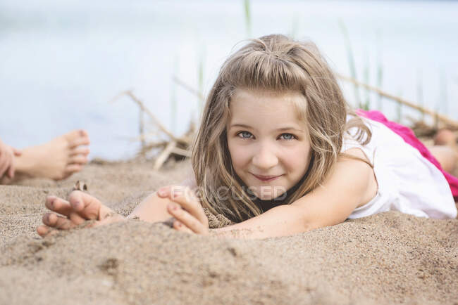 Bambina sdraiata nella sabbia vicino a un lago — Foto stock