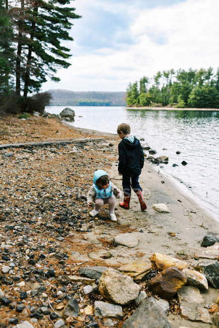 Двое детей у озера собирают камни, чтобы бросить их в воду — стоковое фото