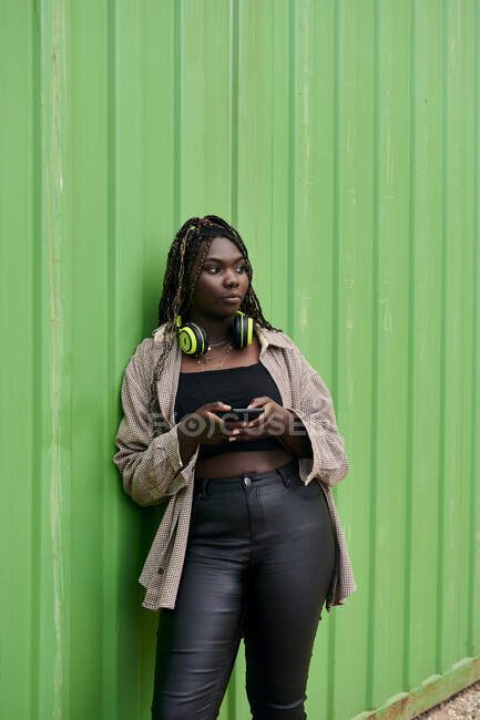 Чорна жінка в міському одязі зі смартфоном і музичними навушниками — стокове фото
