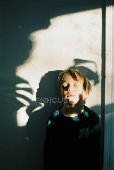 Little boy with shadows across his face and the wall behind him — Stock Photo