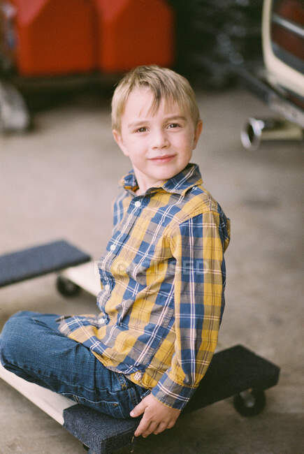 Маленький мальчик сидит на деревянной кукле в гараже своего отца — стоковое фото