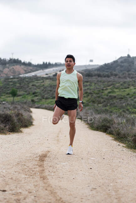 Joven corredor latino calentándose antes de entrenar en el bosque. - foto de stock