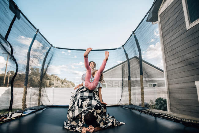 Sisters jumping on a trampoline in the backyard with their dad — Stock Photo