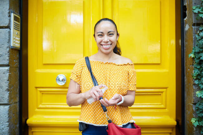 Щаслива молода іспаномовна жінка застосовує дезінфікуючий засіб на вулиці — стокове фото