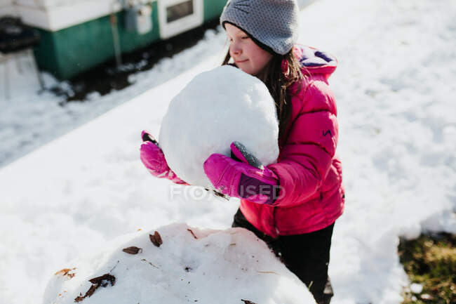 Joven chica construye muñeco de nieve fuera mientras está nevando - foto de stock
