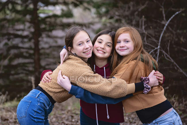Three tween girls standing outdoors hugging each other. — Stock Photo