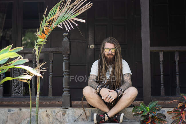 Хіпстер хлопець з дредлоками та татуюванням, що сидить на пляжі в Таліані — стокове фото