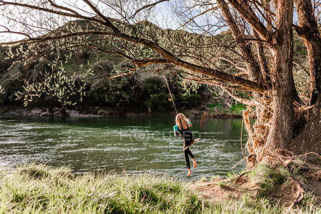 Girl swinging from tree near river in New Zealand — Stock Photo
