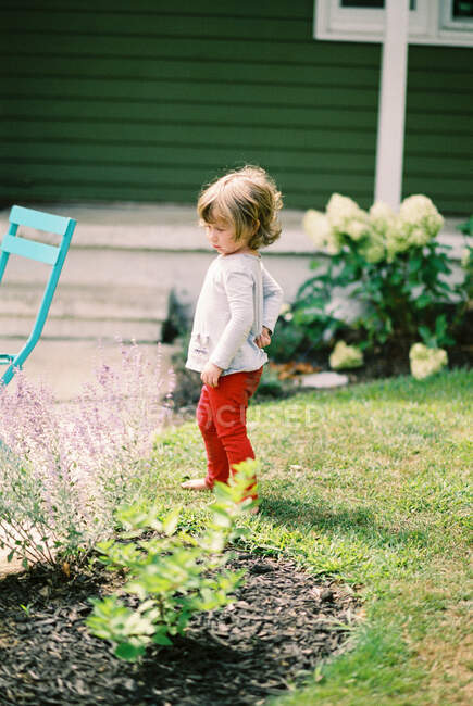 Little girl looking grumpy as she stands in her front yard garden — Stock Photo