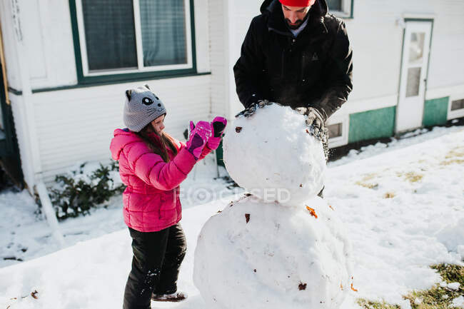 Vater und Tochter bauen Schneemann vor Haus — Stockfoto