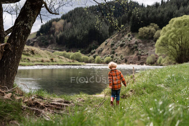 Niño pequeño sosteniendo palo caminando cerca del agua en Nueva Zelanda - foto de stock