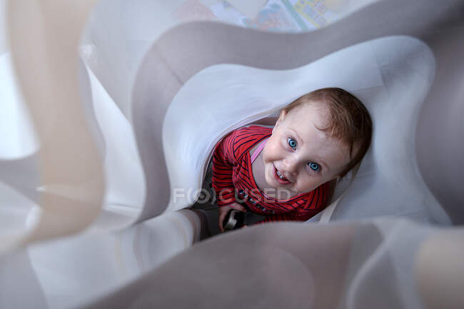 Улыбающаяся маленькая девочка прячется в занавесках — стоковое фото