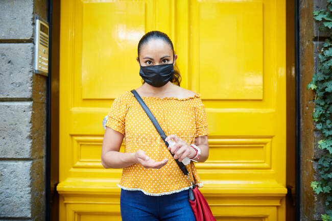 Hispanic woman wearing a face mask and applying hands sanitizer — Stock Photo