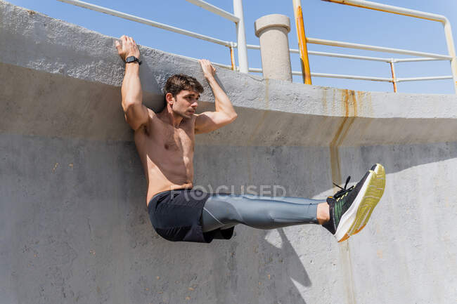 Young man doing sit-ups outdoors hanging on a wall without a shirt — Stock Photo