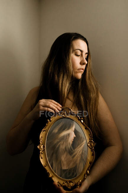 Woman holding a vintage mirror in a room with an image of herself — Stock Photo