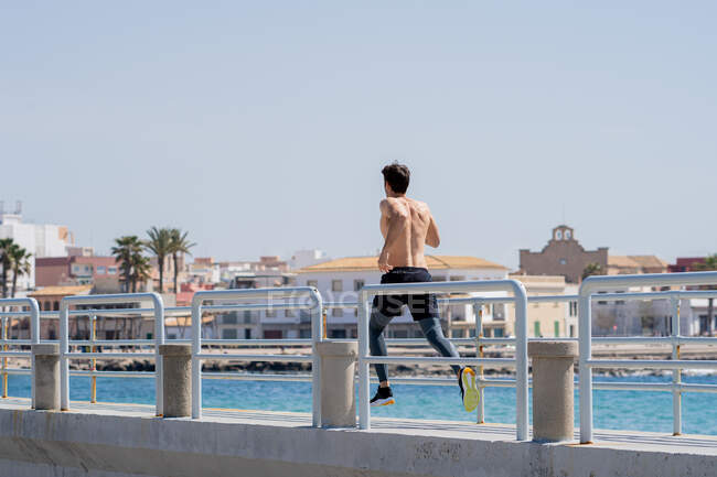 Mann läuft hemdlos auf einer Strandpromenade am Meer, Blick von hinten — Stockfoto