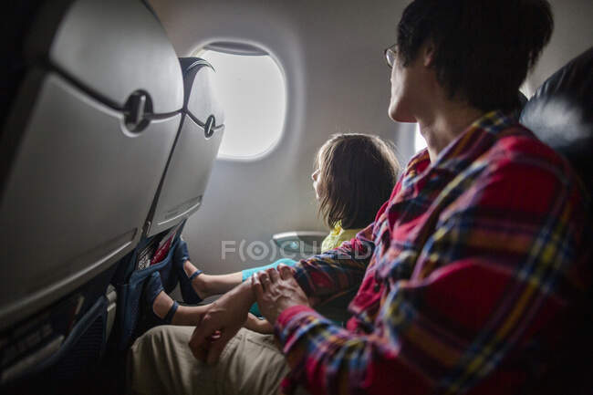 A little girl and father sit together on airplane looking out window — Stock Photo
