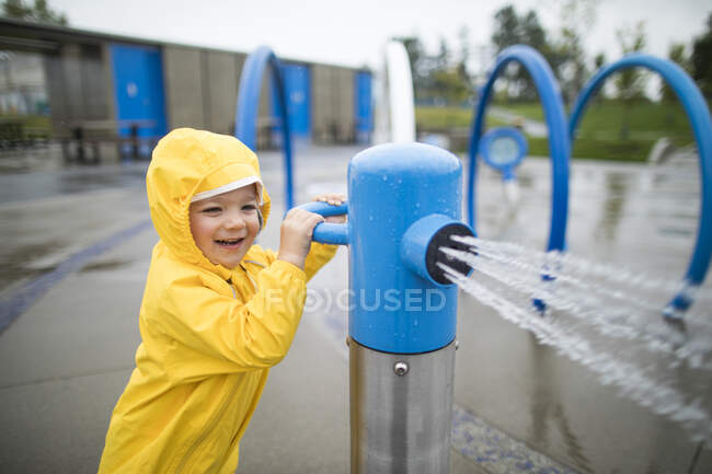 Menino joga no parque aquático em um dia molhado. — Fotografia de Stock