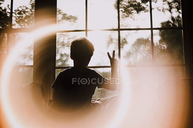 Back of Young Boy in Window Making Peace Sign With Circle Light Effect — Stock Photo