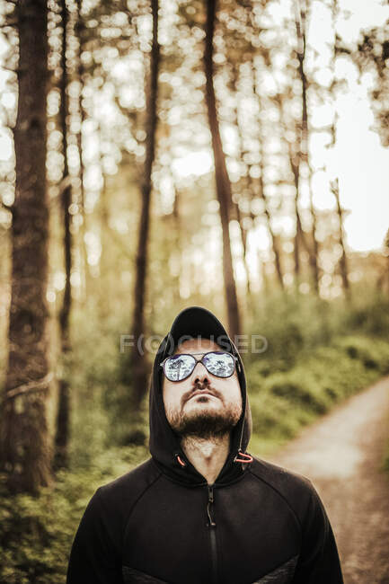 Uomo con occhiali da sole e cappuccio in una bellissima foresta — Foto stock